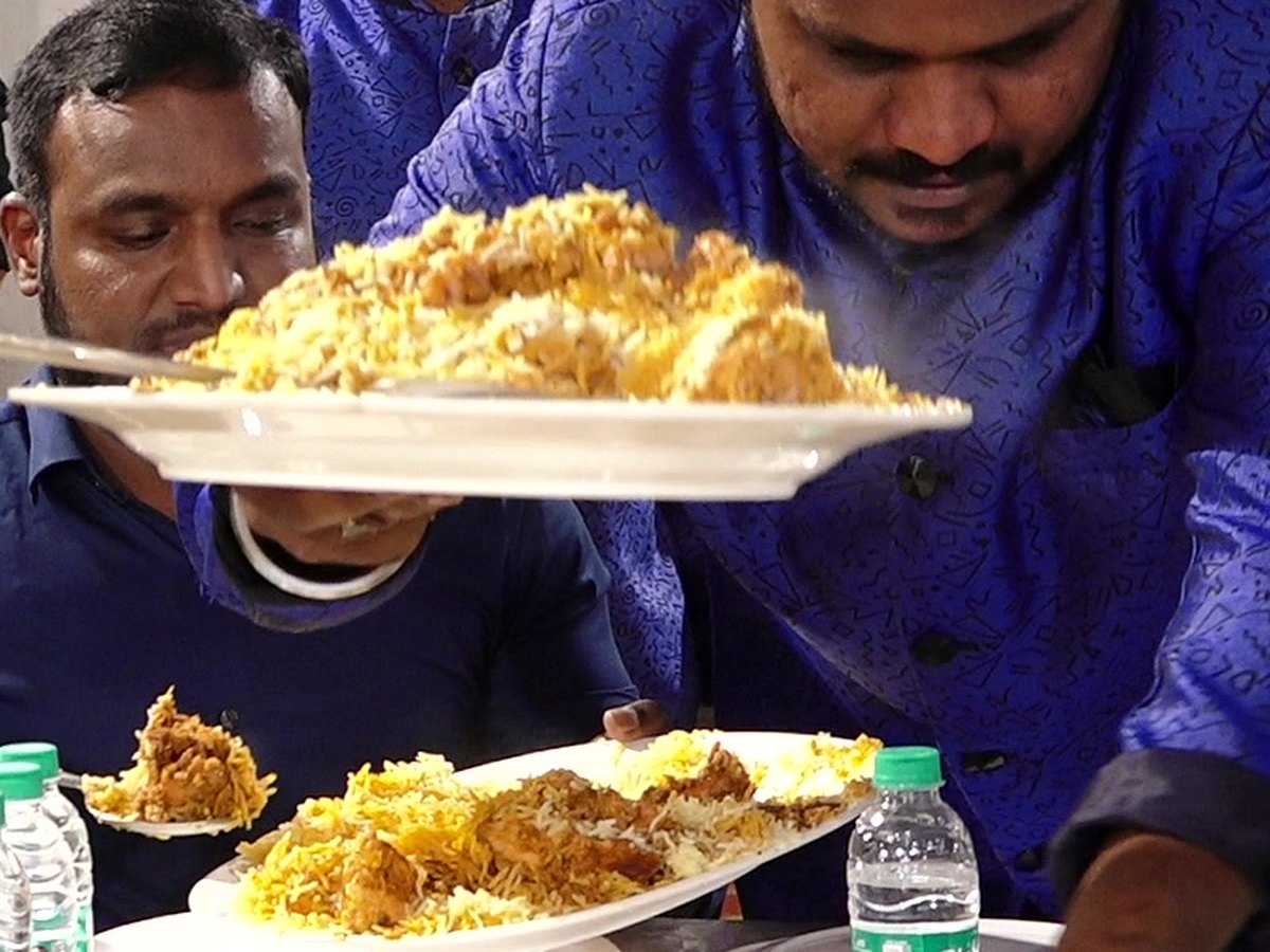 Zarafé server in blue uniform bringing a platter of dum biryani to a guest table